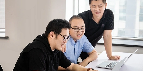 Three men working together on laptops in a bright office space.